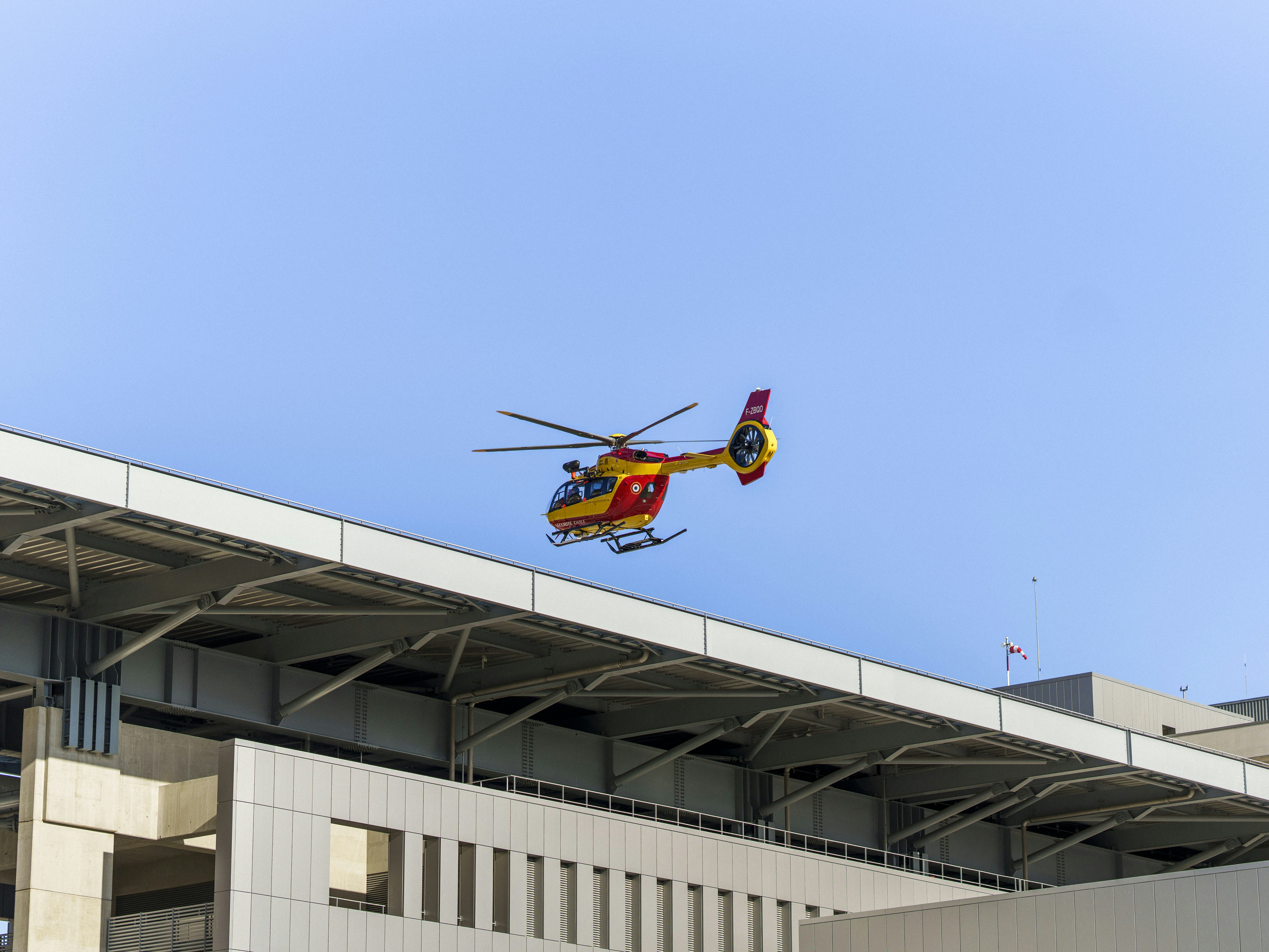 a red and yellow helicopter flying over a building, 
