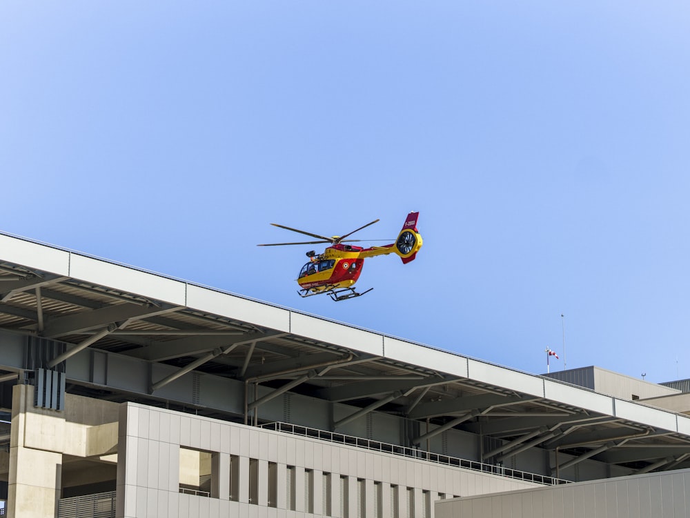 a red and yellow helicopter flying over a building