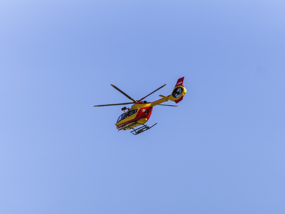 a red and yellow helicopter flying through a blue sky