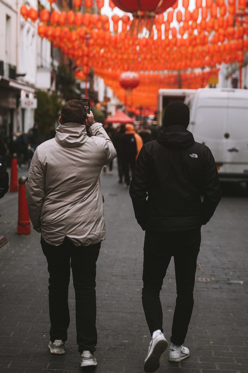 two people walking down a city street under orange lanterns