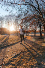 A runner jogging through a leafy park trail at sunrise.