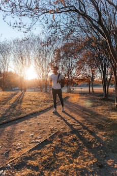 A person jogging in a sunny park surrounded by green trees and blue sky.