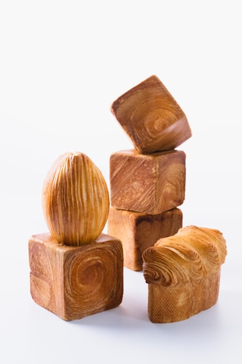 Several artistic wooden objects with intricate swirling patterns are arranged together. The objects include cube shapes with circular patterns and an elongated egg-shaped object. A piece resembling a wave or textured curve adds variety to the arrangement. The light-colored wood showcases the detailed grain, creating an engaging visual texture against a plain background.