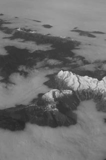 A dramatic aerial capture of a mountain range with snow-capped peaks piercing through low-hanging clouds.