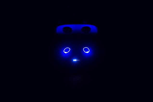 A dark background with a few illuminated blue elements that resemble eyes and a horizontal line of small dots beneath them, suggesting a robotic or technological theme.
