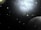 A vast and dark space scene peppered with numerous small celestial objects resembling stars and planets. A large, bright nebula dominates the upper part of the image, casting a diffuse glow against the black backdrop. In the lower right corner, a prominent planet is partially visible, appearing spherical and shaded in gray.
