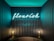 A cozy alcove with dark vertical paneling features a neon sign displaying the word 'flourish'. The soft glow of the neon is complemented by two delicate lamps placed on either side, casting warm light.