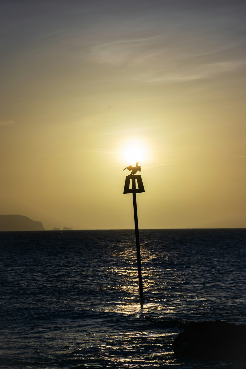 the sun is setting over the ocean with a pole sticking out of the water