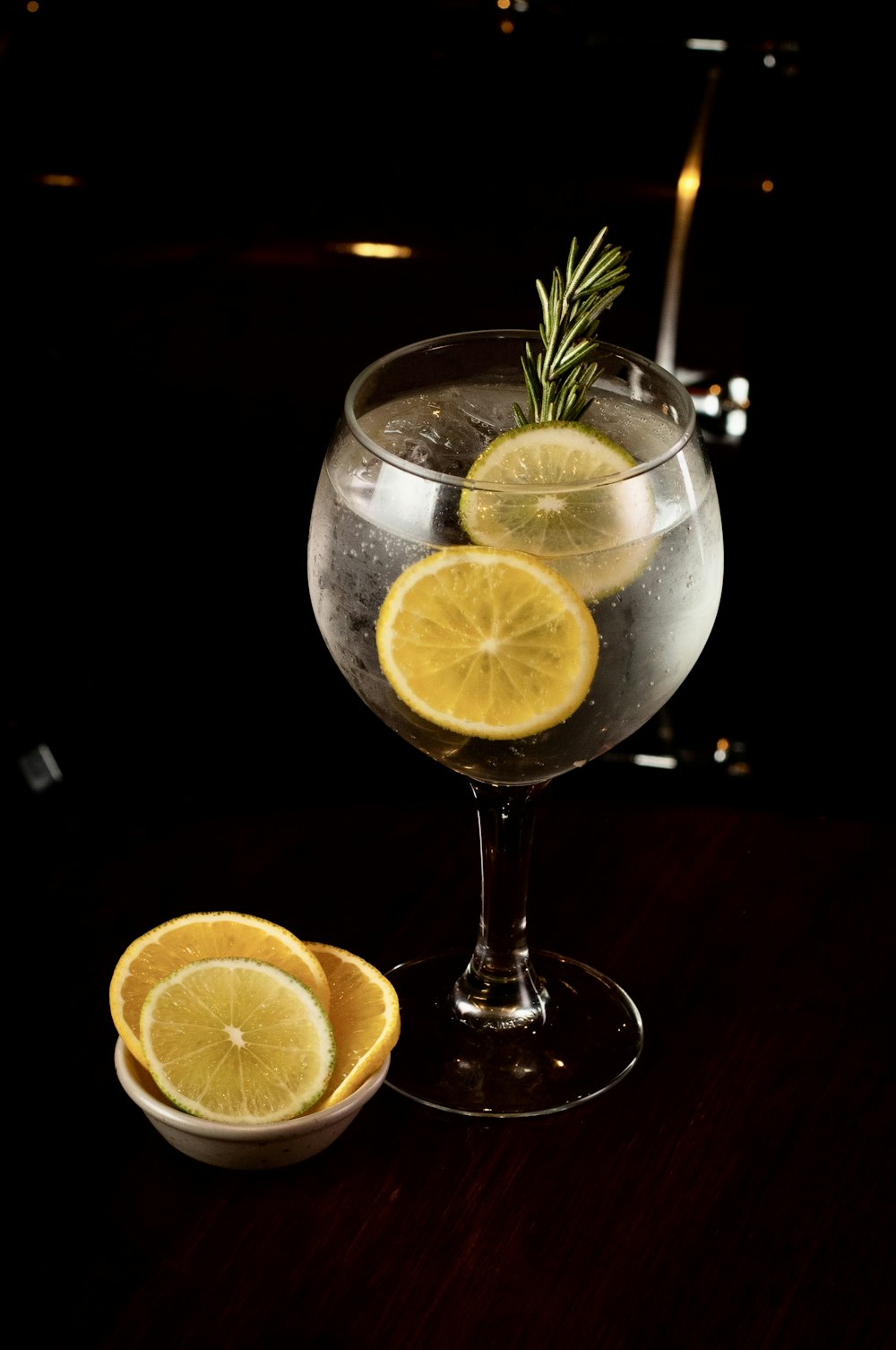 a glass of wine with lemons and a rosemary sprig