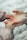 A close-up of two hands, one larger and one smaller, gently holding each other. The setting seems gentle and caring, highlighting a protective or nurturing relationship. The background is blurred, focusing attention on the hands.