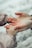 A close-up of two hands, one larger and one smaller, gently holding each other. The setting seems gentle and caring, highlighting a protective or nurturing relationship. The background is blurred, focusing attention on the hands.