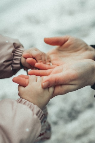 A close-up of two hands, one larger and one smaller, gently holding each other. The setting seems gentle and caring, highlighting a protective or nurturing relationship. The background is blurred, focusing attention on the hands.