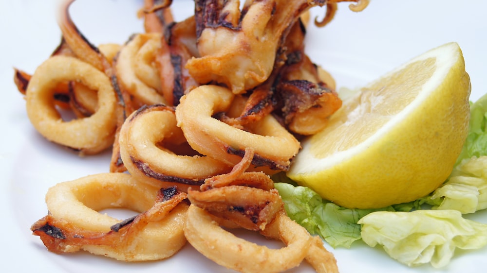 a white plate topped with fried squid rings next to a lemon wedge