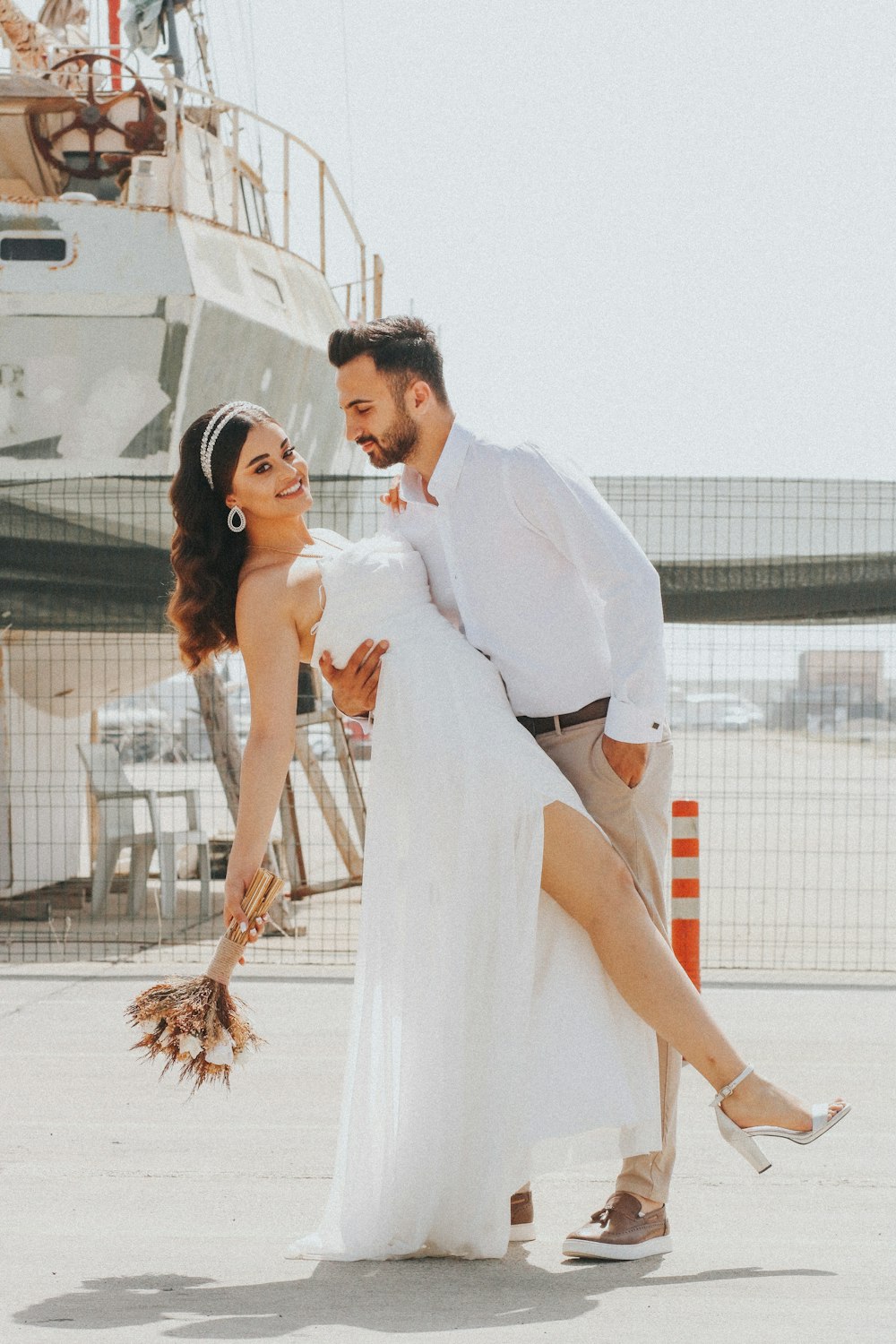 a bride and groom pose for a photo in front of a boat