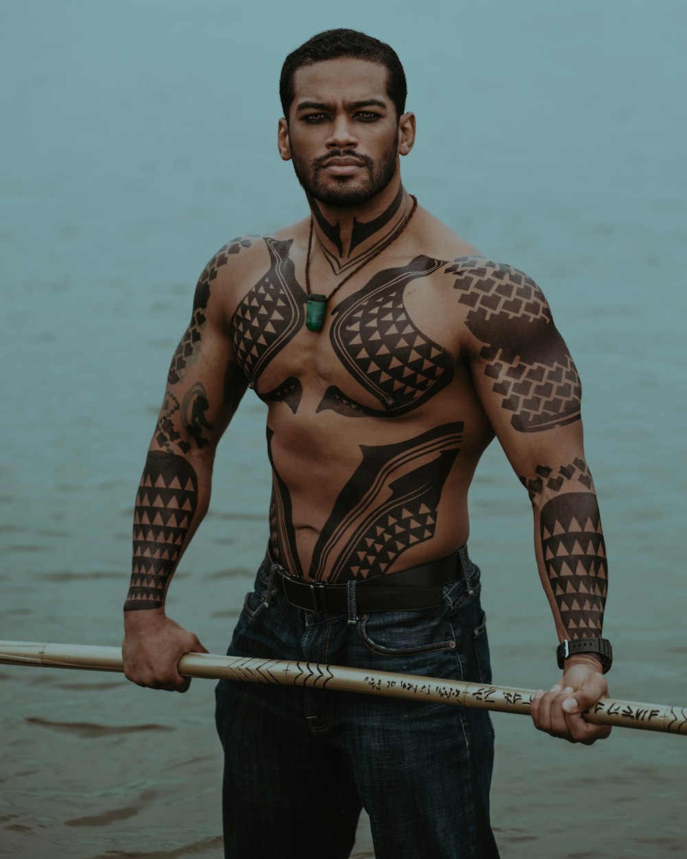 a man with tattoos on his chest holding a stick