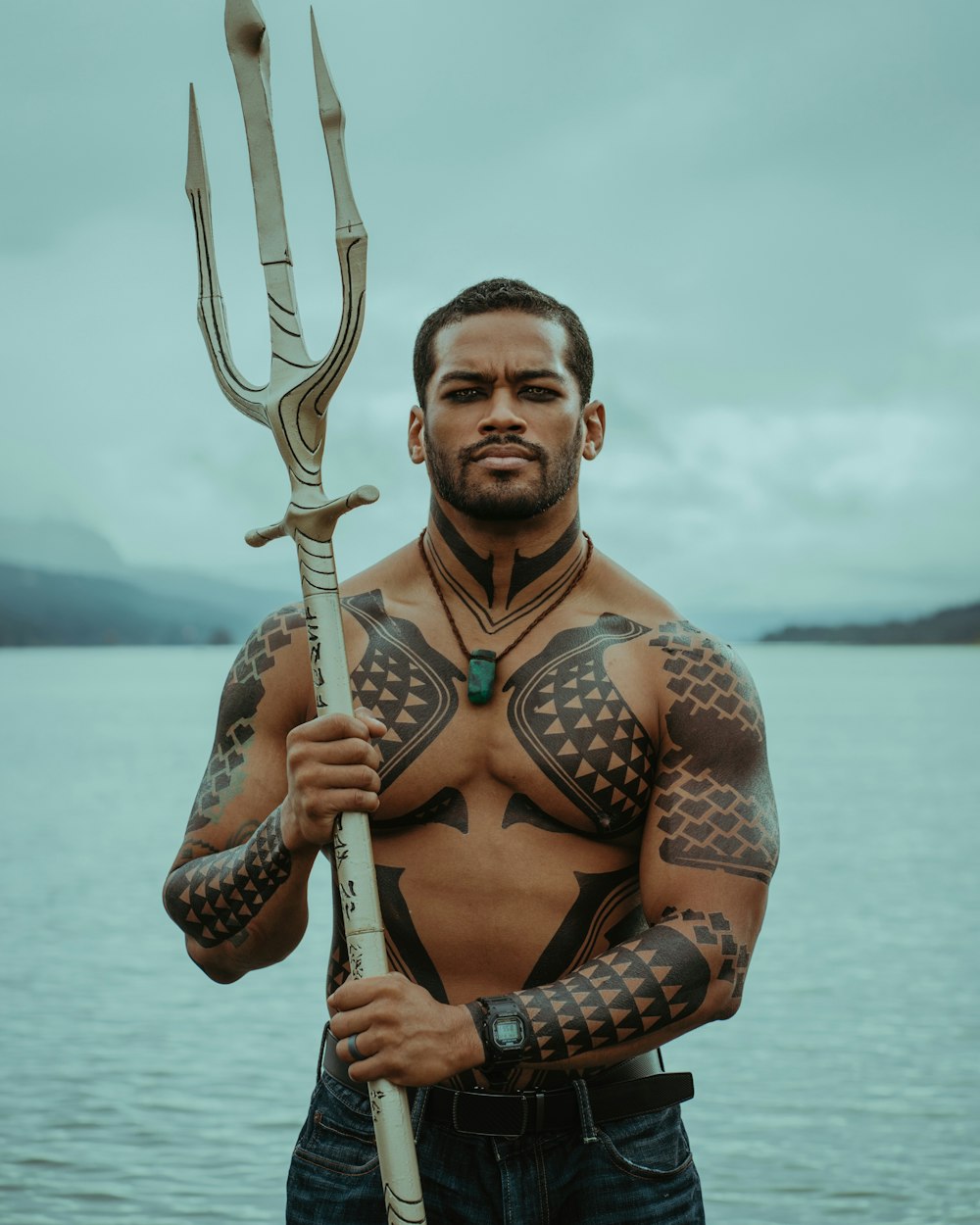 um homem com tatuagens segurando uma lança grande