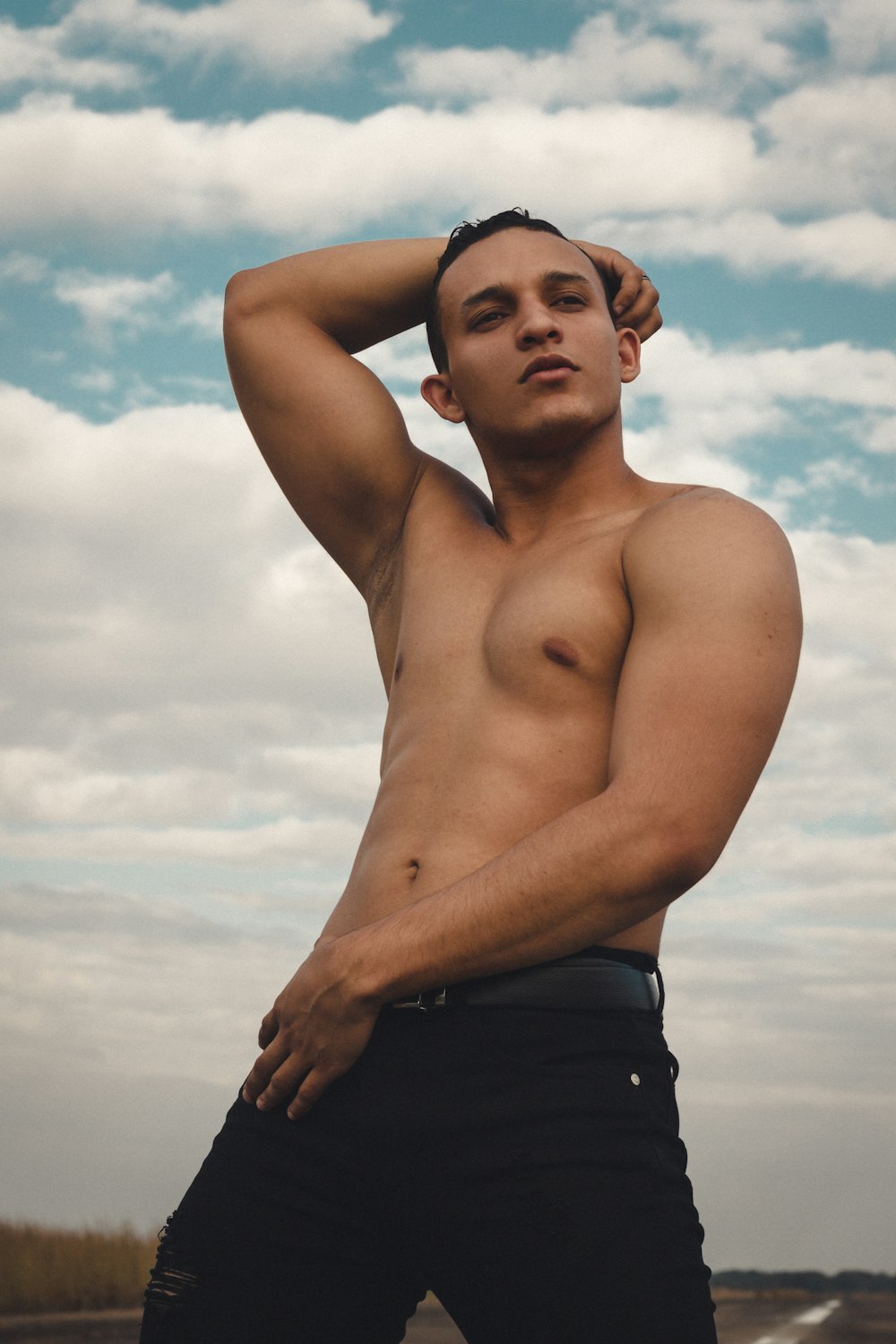 a shirtless man standing in front of a cloudy sky