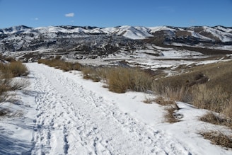 A serene mountain trail winding through snow-capped peaks under a clear blue sky.
