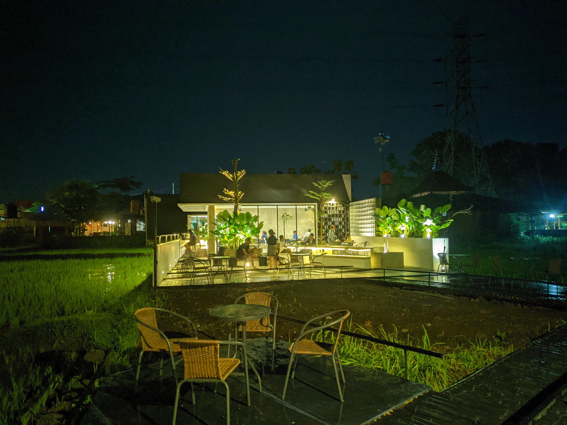 The inviting outdoor seating area of Ilios Cafe, surrounded by lush greenery and soft string lights, perfect for a relaxed evening meal.