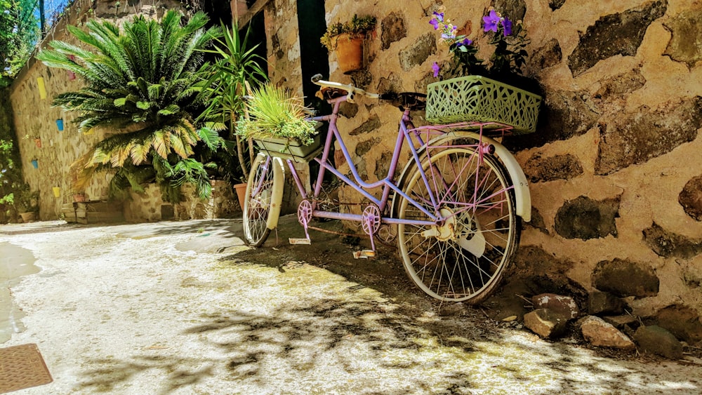 a purple bike parked next to a stone wall