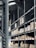 Shelving units filled with stacked boxes and pallets in a warehouse-like environment. The shelves are tall and extend into the distance, creating an orderly and spacious atmosphere. Overhead, industrial lighting and structural elements are visible.