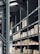 Shelving units filled with stacked boxes and pallets in a warehouse-like environment. The shelves are tall and extend into the distance, creating an orderly and spacious atmosphere. Overhead, industrial lighting and structural elements are visible.