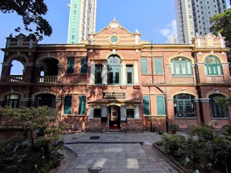 A historic two-story brick building with beautiful architectural details, featuring arched windows and columns. It is surrounded by trees and plants, creating a peaceful courtyard setting.