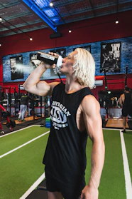 Close-up of a muscular man holding a protein shaker in a gym setting with vibrant lighting.