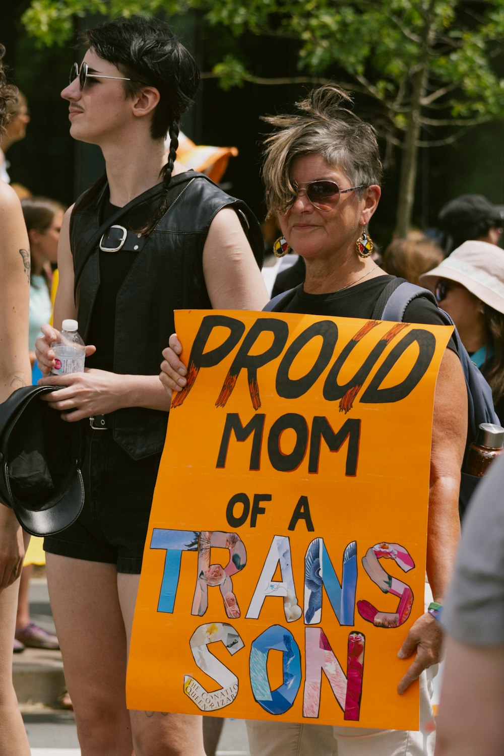 a woman holding a sign that says proud mom of a transs son