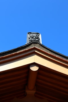 A traditional rooftop featuring intricate architectural details, with a decorative emblem positioned at the peak against a clear blue sky.