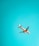 A commercial airplane is flying against a backdrop of a clear turquoise sky. The aircraft appears to have a colorful design on its tail and engines, with visible landing gear partially extended.