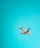 A commercial airplane is flying against a backdrop of a clear turquoise sky. The aircraft appears to have a colorful design on its tail and engines, with visible landing gear partially extended.