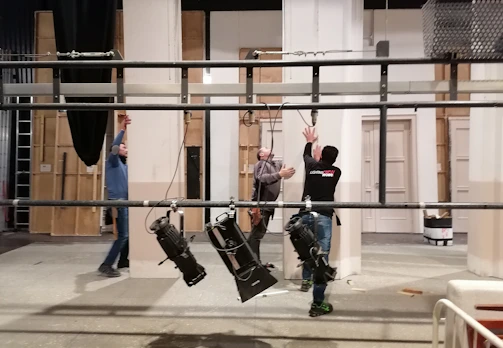 A behind-the-scenes view of a gaffer adjusting a complex lighting rig on a film set at dusk.