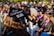 A group of people wearing black graduation caps and gowns sit outdoors, attending a graduation ceremony. The focus is on a cap with the phrase 'I'm a Social Worker! What's your superpower?' written on it. Sunlight casts a warm glow over the scene, highlighting the joyous atmosphere.