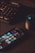 A smartphone displaying various social media app icons is placed on a dark surface. Nearby, a gaming mouse with a glowing logo and a mechanical keyboard with illuminated keys are visible. The lighting is low and focused, creating a moody atmosphere.