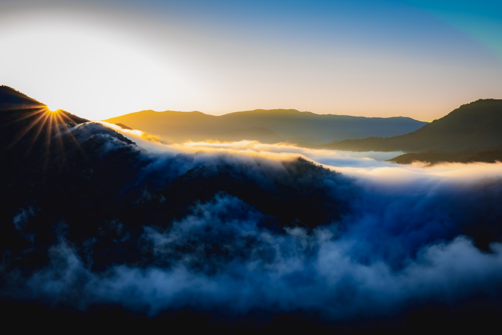 the sun shines brightly above the clouds in the mountains