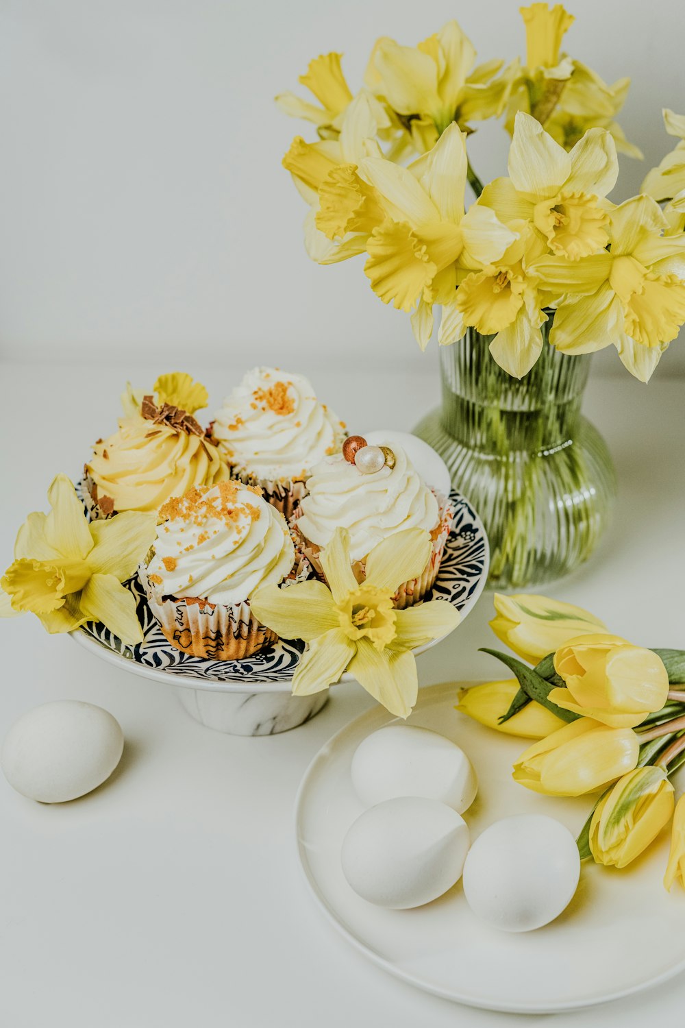 a white plate topped with cupcakes next to yellow flowers