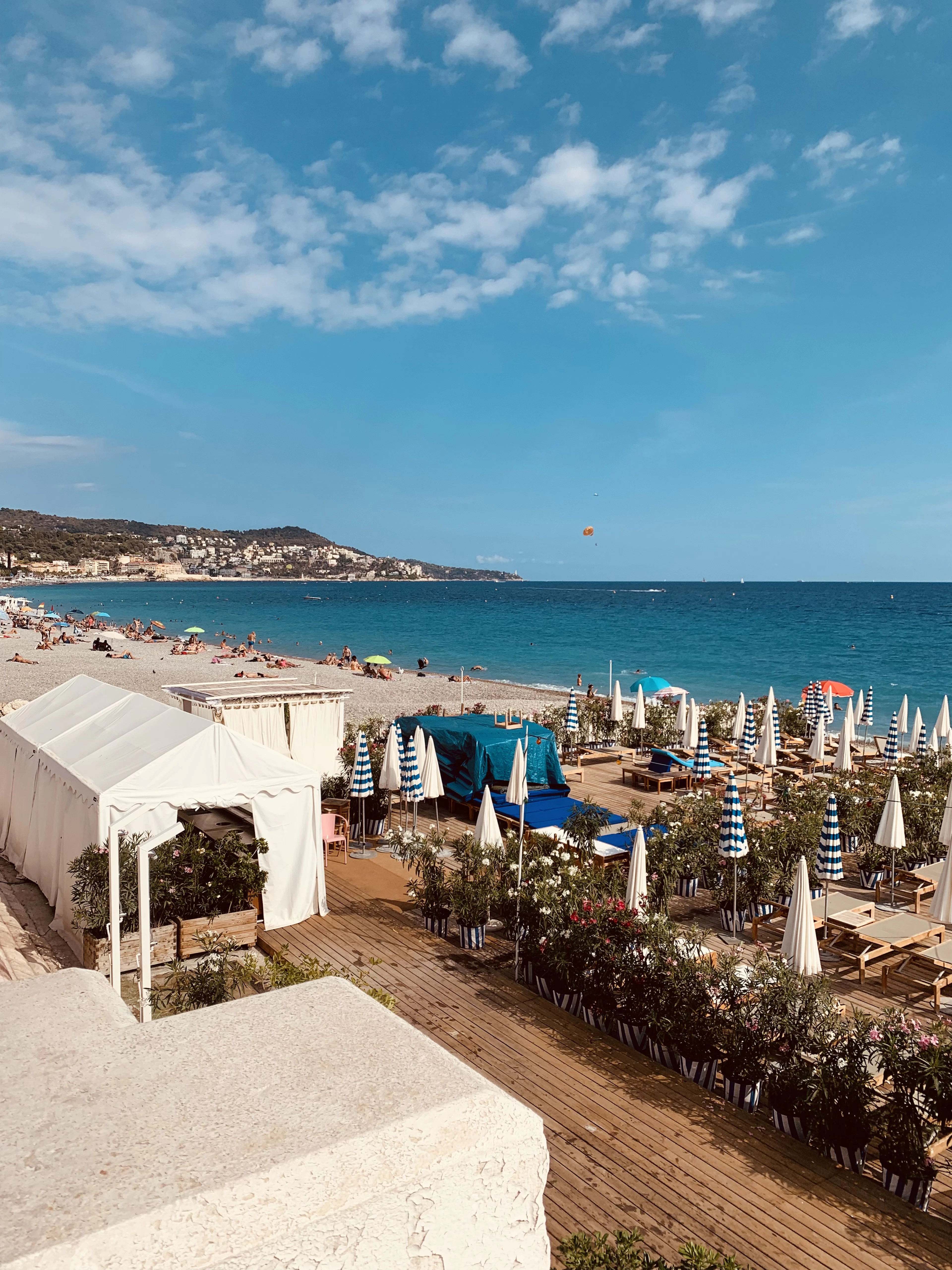 Elevated view over a beach club with striped umbrellas and sun loungers along Nice's curving bay.