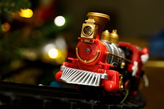 a red toy train on a track near a christmas tree