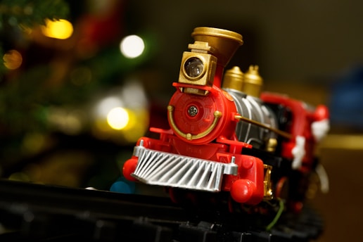 a red toy train on a track near a christmas tree