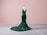 A dark green, sequined evening gown displayed on a mannequin. The gown features a form-fitting, mermaid silhouette with a dramatic train, set against a soft pink background and gray carpeted floor.