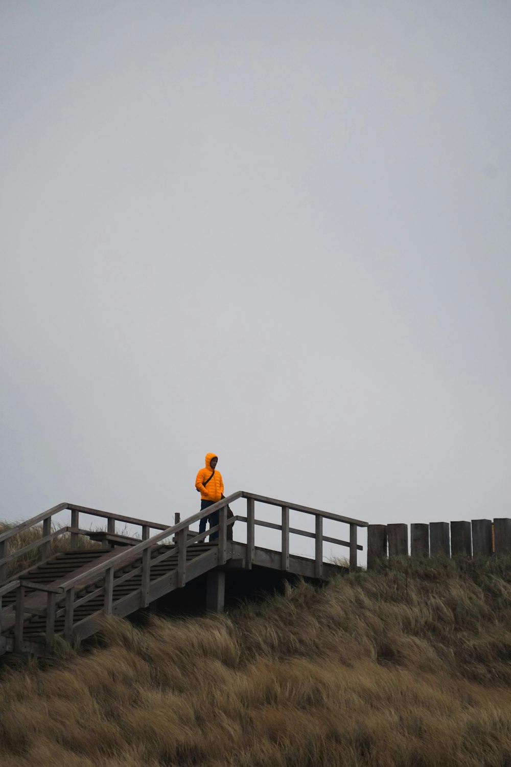 a man in an orange jacket standing on a wooden bridge