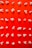 Popcorn is neatly arranged in a grid pattern on a bright red background, creating a visually striking contrast. Each kernel is distinct, with different shapes and sizes, highlighting the irregular nature of popcorn.