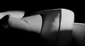 Three overlapping cushions with textured fabric are positioned in a dimly lit environment. The play of light and shadow highlights the texture and contours of the cushions, creating a stark contrast between light and dark areas.