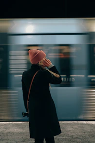 a woman in a black coat and a red hat is talking on a cell phone