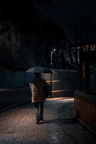 A lone figure with an umbrella walking past a row of glowing vending machines at night.