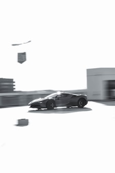 A sleek sports car is captured in motion, appearing to speed across an empty area with blurred surroundings. The image is predominantly in shades of gray, giving it a modern and dynamic feel.
