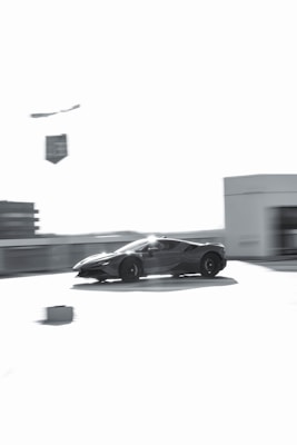 A sleek sports car is captured in motion, appearing to speed across an empty area with blurred surroundings. The image is predominantly in shades of gray, giving it a modern and dynamic feel.
