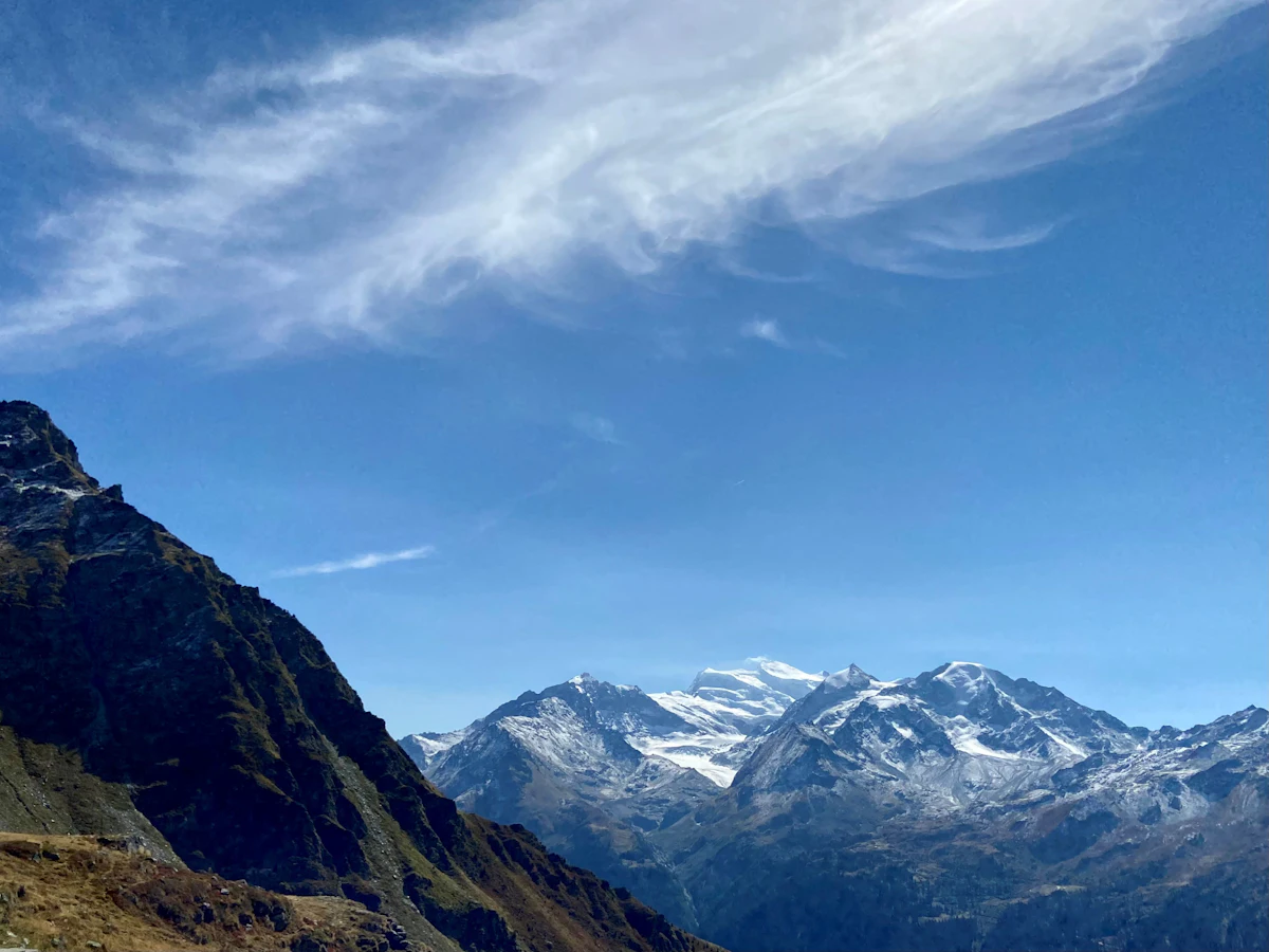 Snow-capped peaks above a dark ridge in the Val de Bagnes, under a blue sky