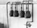 A black and white image of four large, industrial gas meters mounted on a concrete wall with visible piping and connections. The setup is located indoors or in an industrial area, and a section of brickwork is visible above the concrete.
